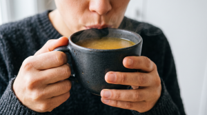 Close-up of hands holding a mug of bone broth raised to the lips, tasting its savory flavor